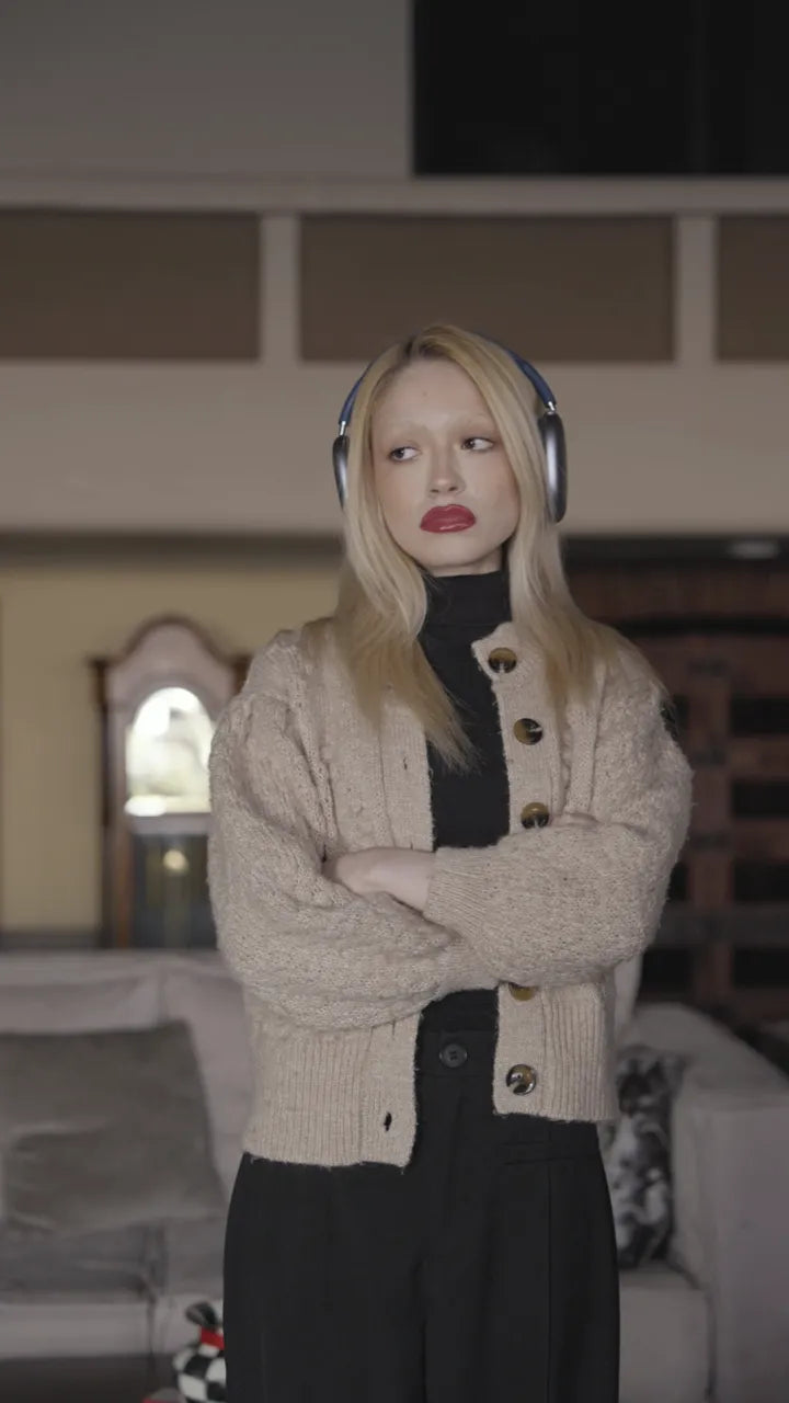 A woman standing in a living room wearing over-ear headphones, unimpressed